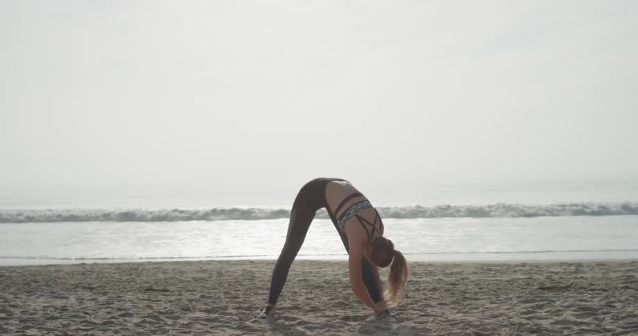 A woman does yoga and stretches on the beach