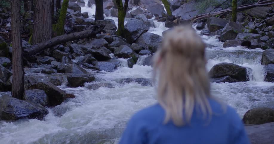 A woman watches the water crash over the rocks of the stream