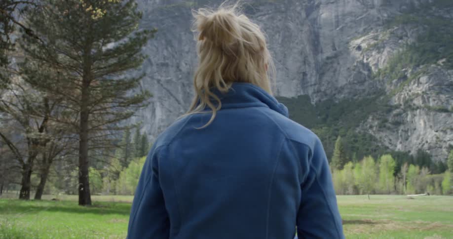 A woman is drinking from a water bottle as she takes in a view of a waterfall