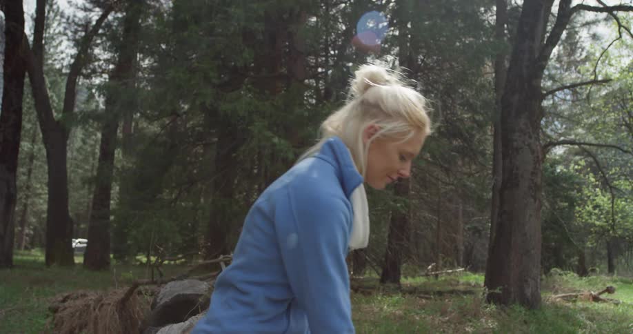 A woman sitting on a log reaches down to grab a water bottle