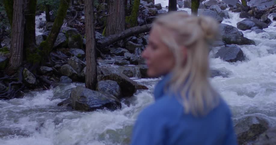 A woman stands next to a river in a forest