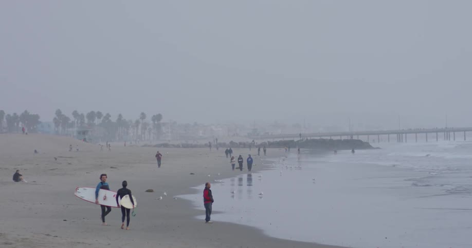 Surfers walk on a beach on a misty day