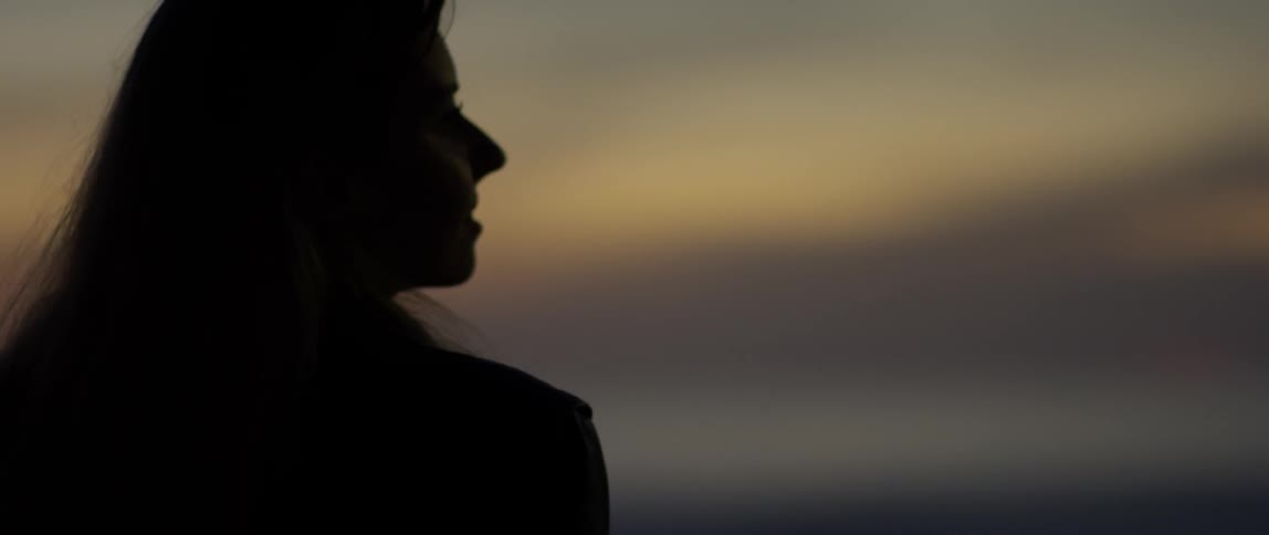 A woman stands outside at sunset