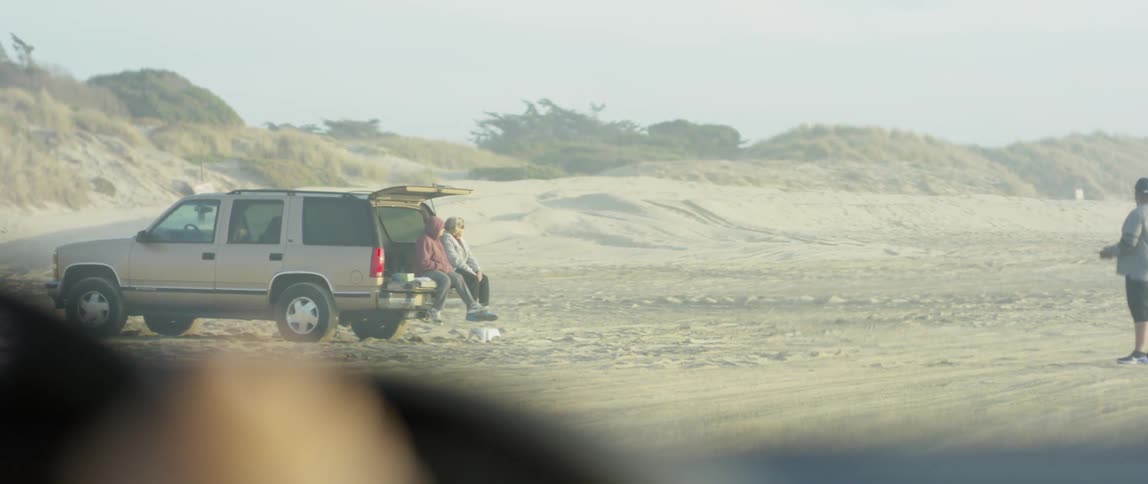 A car drives by a man flying a toy airplane on a beach
