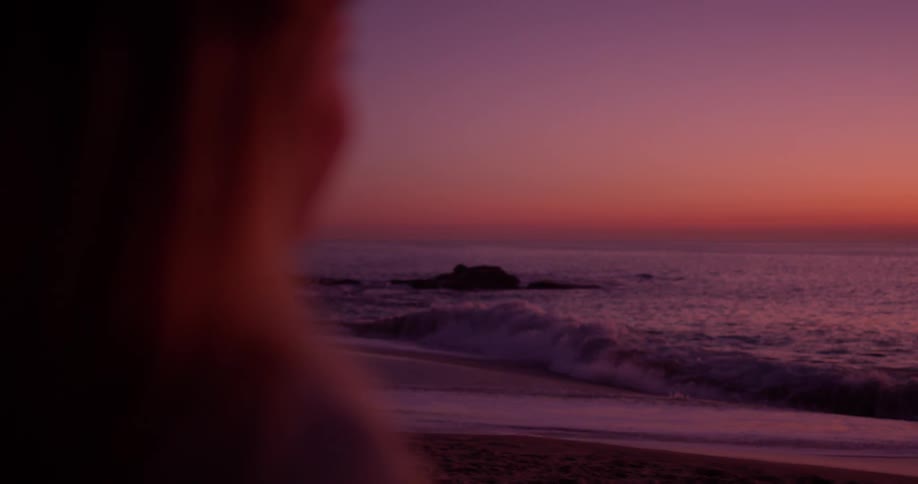 A woman watches the waves hit the shore at dawn