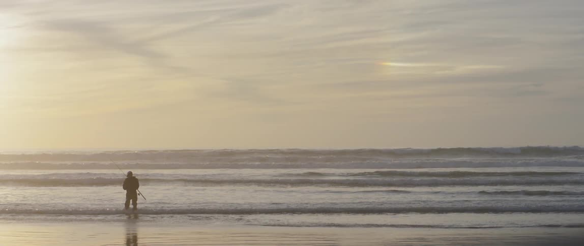 A fisherman stands on a beach at sunset