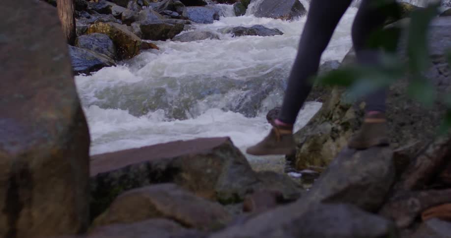 A woman walks on rocks near a flowing stream