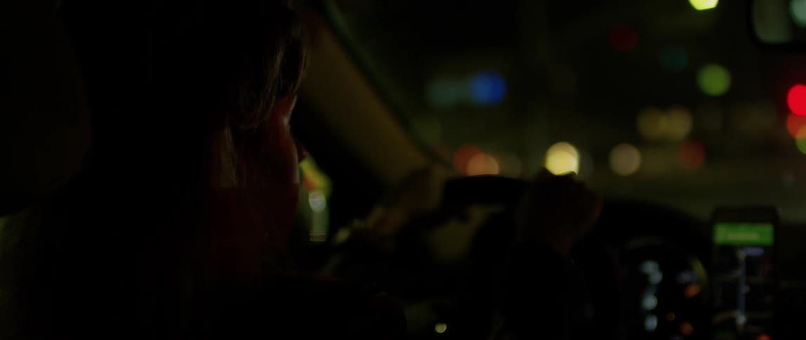 A woman drives a car in a city at night