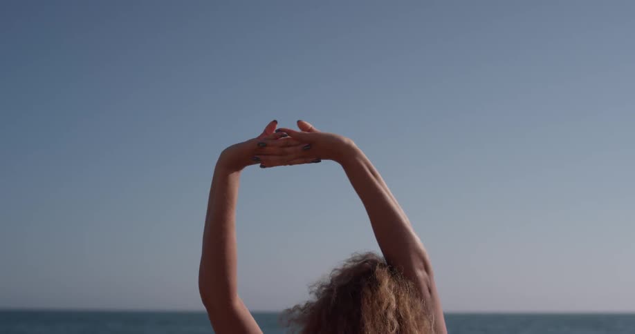 A woman stretches her arms up on the beach