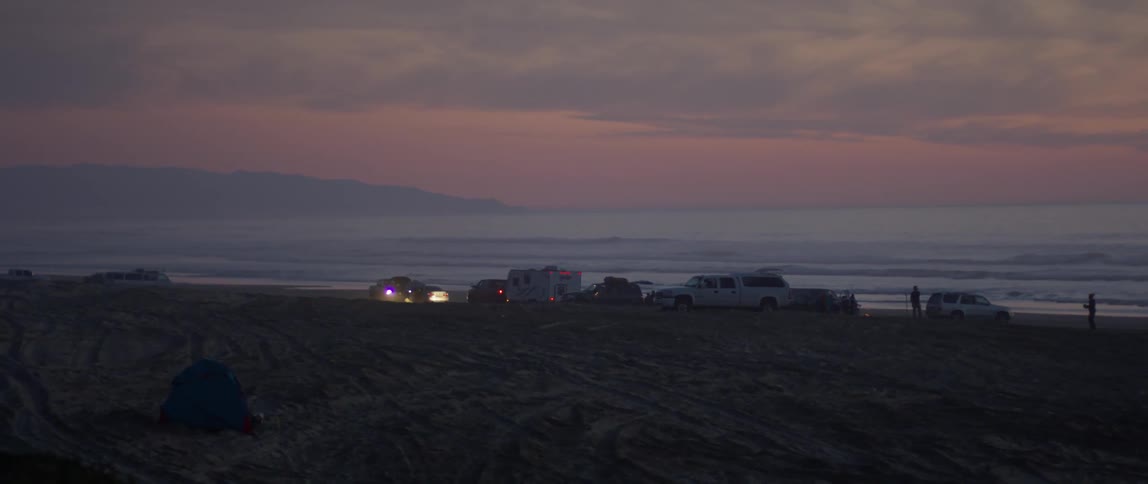 Several vehicles parked on the beach at sunset