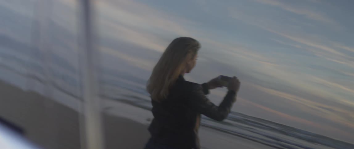 A woman photographs a beach at sunset