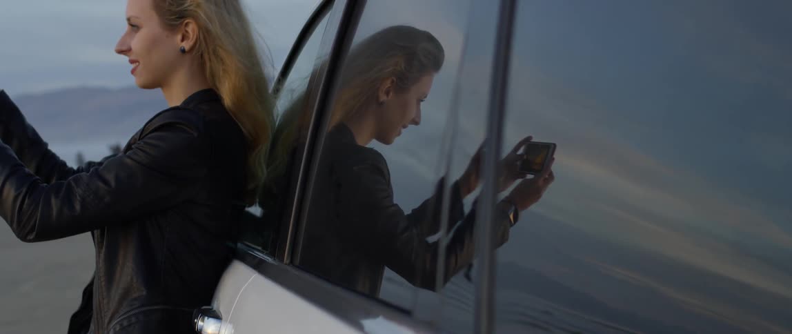 Smiling woman leans against a vehicle and takes a picture