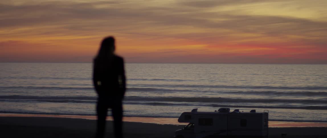 The person walks over to the water at dawn