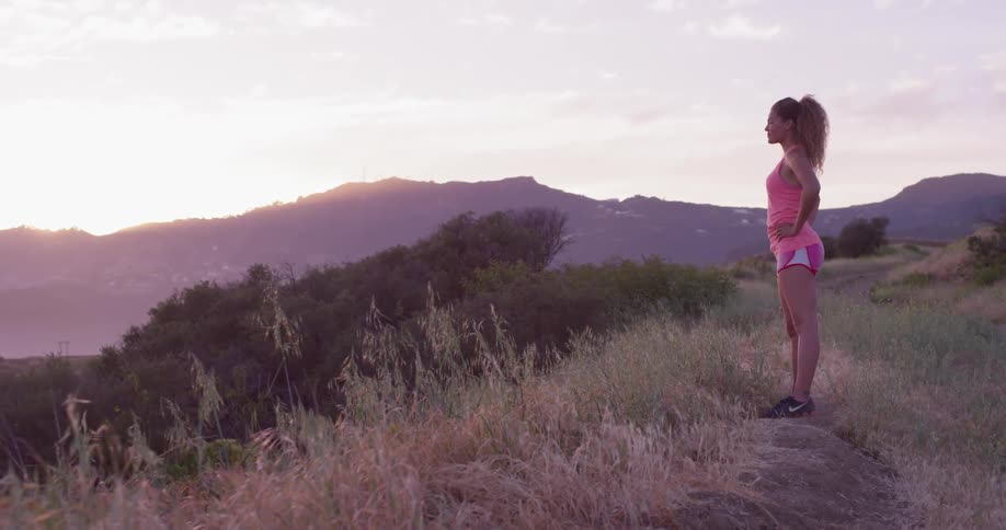 A woman stands on the mountain top at sunset