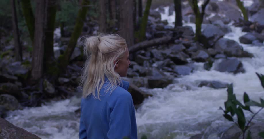 A woman standing near a river smiles as she looks up