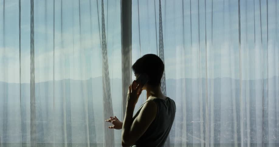 A woman talks on a phone in front of a window