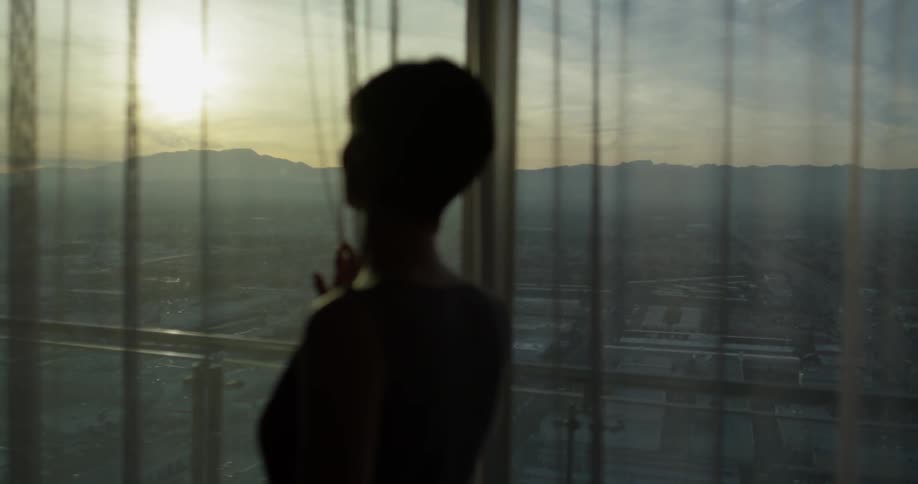 A woman looks out a window at sunset