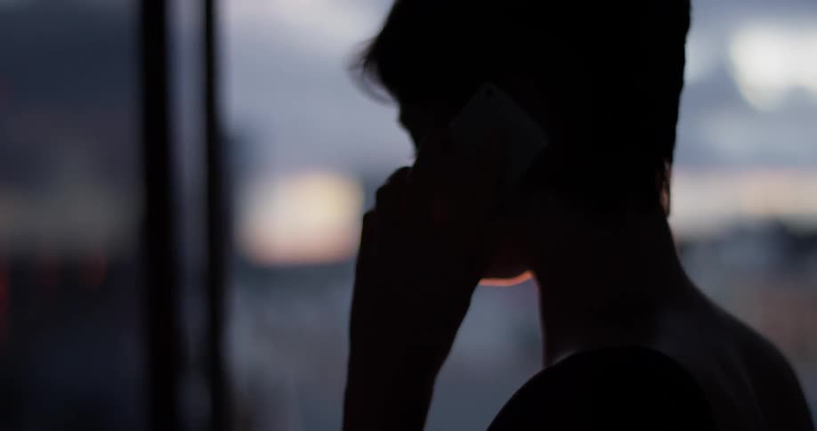 A woman talks on the phone as the sun sets over the city
