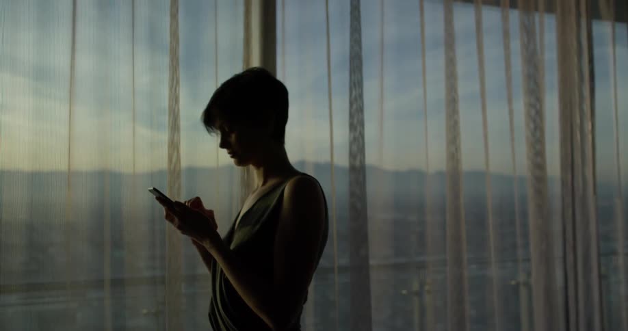 A woman is using her phone in front of the drapes
