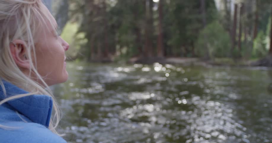 A woman stands next to a river in a forest
