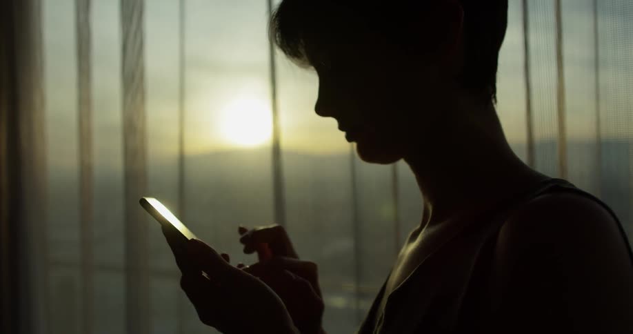 A woman checks her phone at sunset