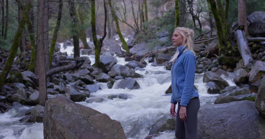 A woman watches the stream in the woods