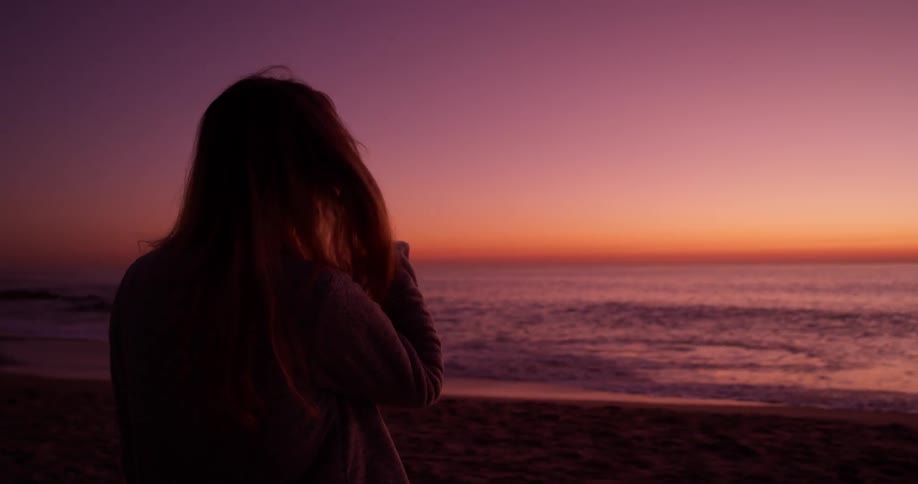 Woman smiles as she looks out at the ocean at sunset