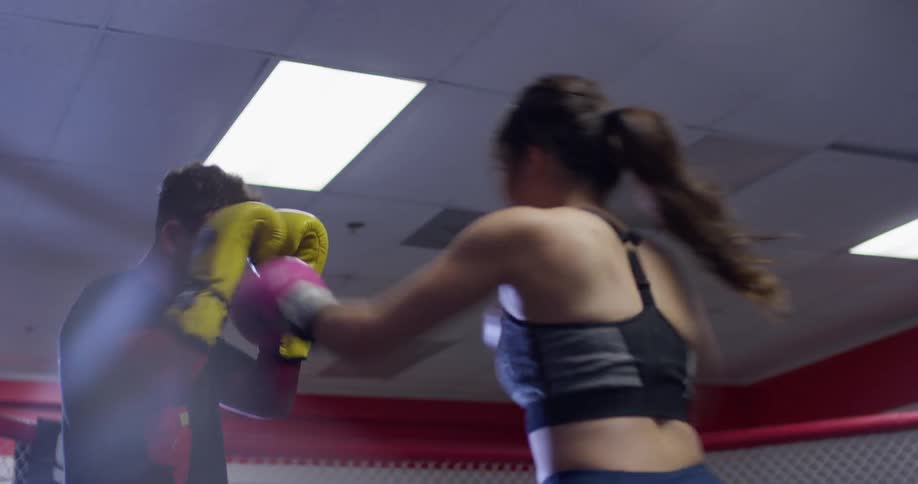 Woman practices boxing with a man in a boxing ring