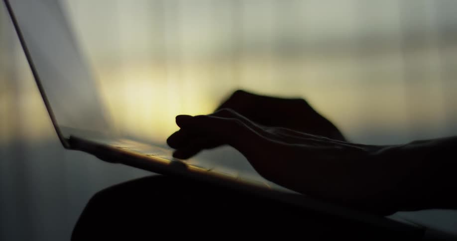 A person types on a laptop at sunset