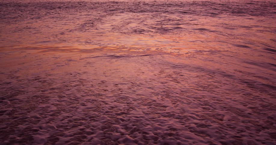 A wave slowly hits the shore at dawn
