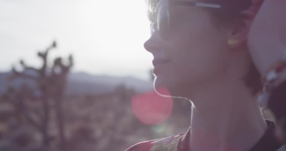 Woman wearing sunglasses rubs her head as she stands in a field
