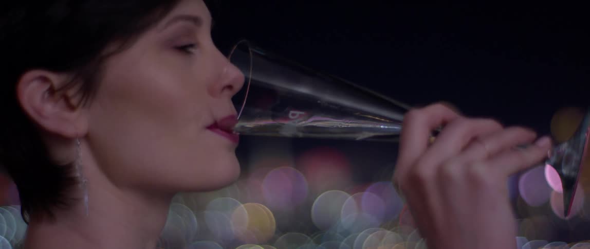 Woman takes a sip out of a glass while looking out at the city at night