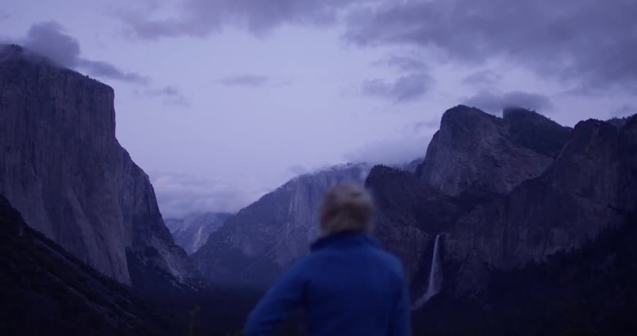 The woman looks out over the mountain range on a cloudy day