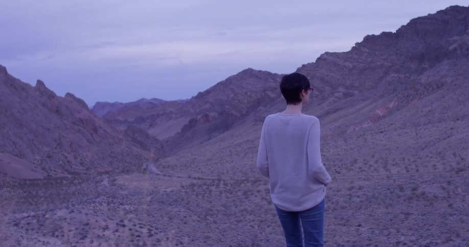 A woman walks in a desert and stops to look around