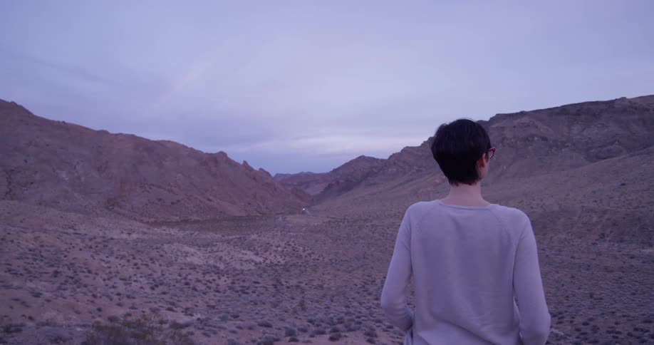 Woman looks out over brushy hilly desert