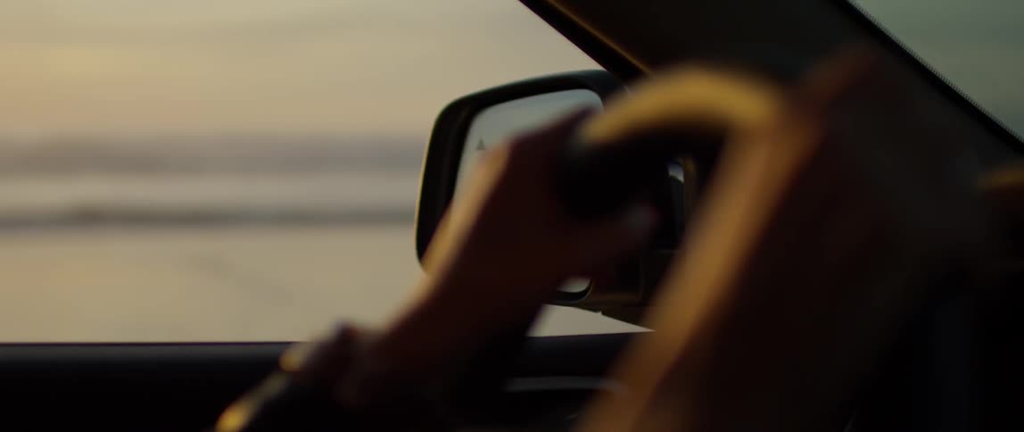 A person steers a car past a woman standing on the beach
