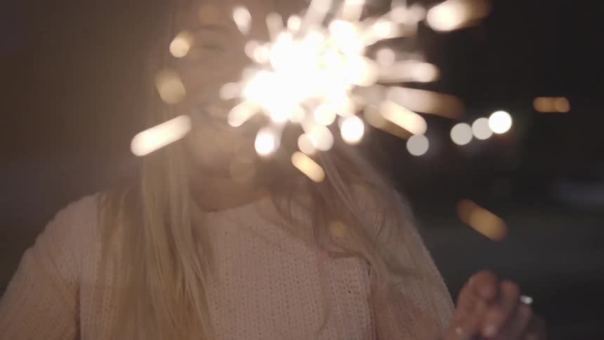 A woman smiles while holding burning sparklers at night