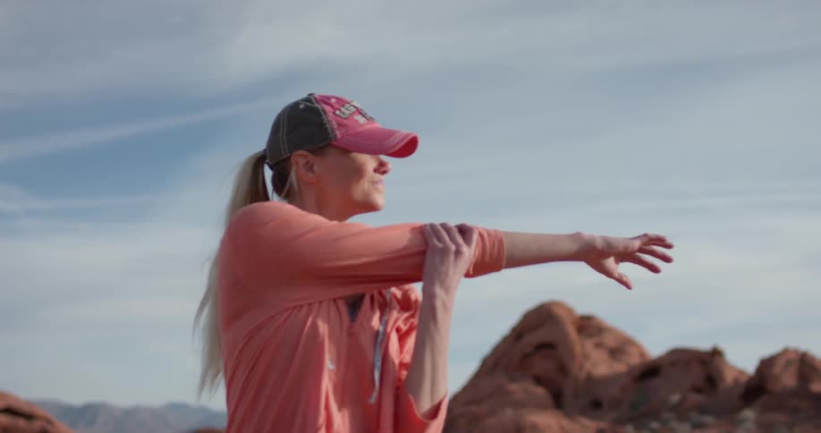 Woman stands stretching her arms outside looking out over rocky hills