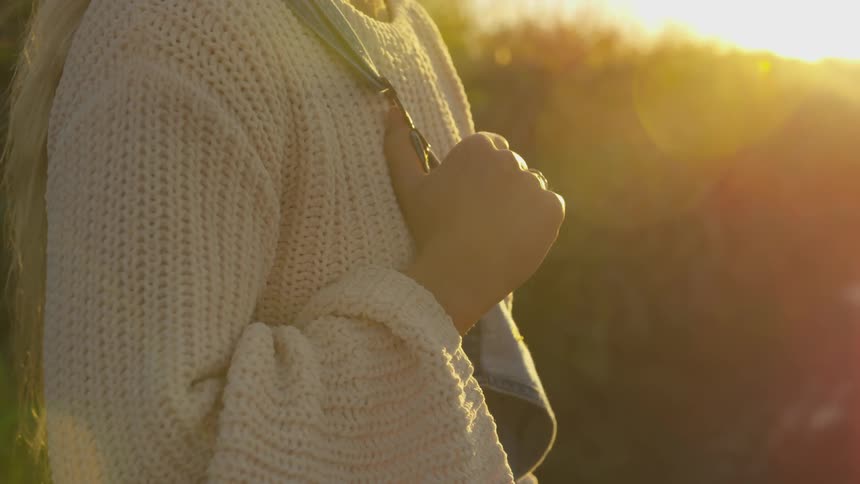 A woman is holding her overalls at sunset