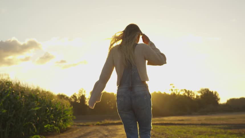 Woman walks in a field next to crops on a sunny day