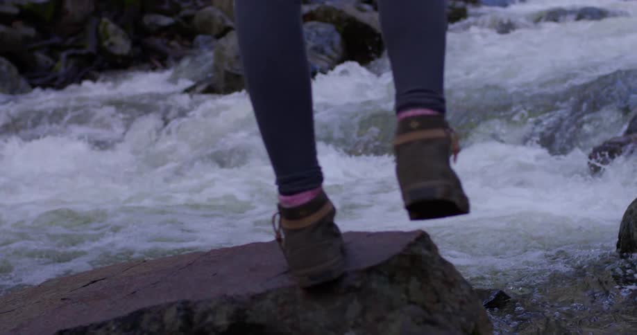 A woman stands on a rock next to a river
