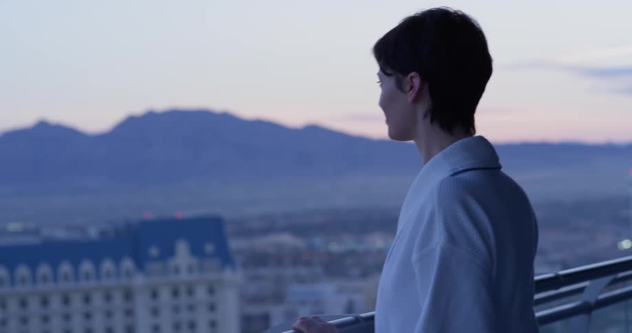 A woman stands on a hotel balcony at sunset