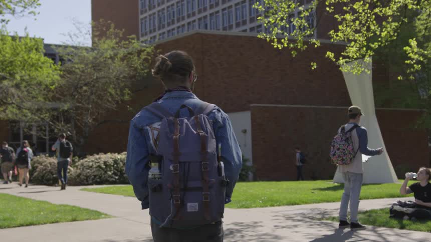 A man is walking on a college campus carrying a backpack on a sunny day