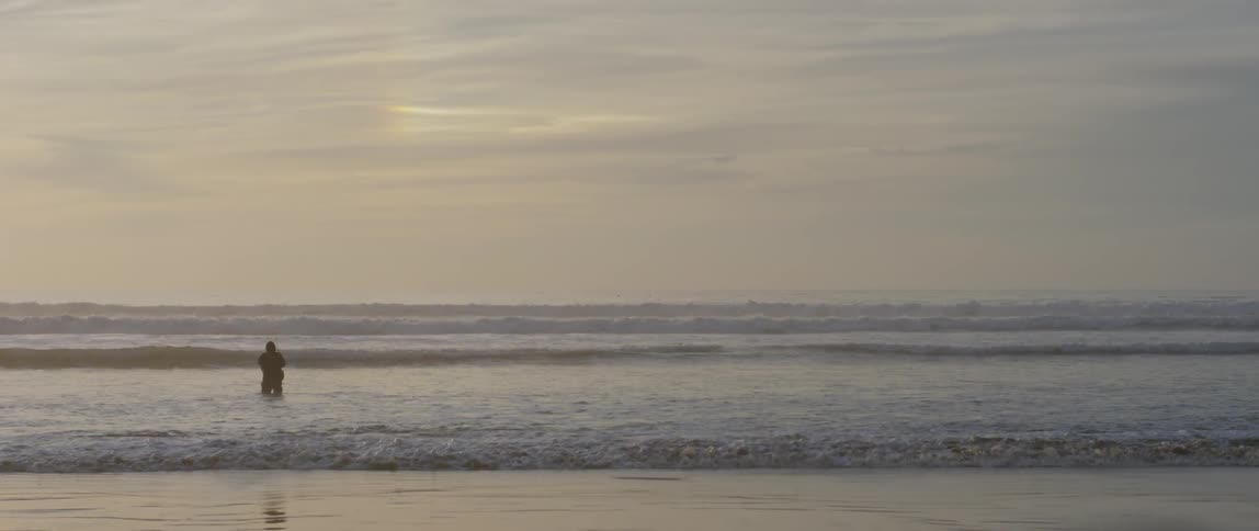 A fisherman wades in ocean water on a beach