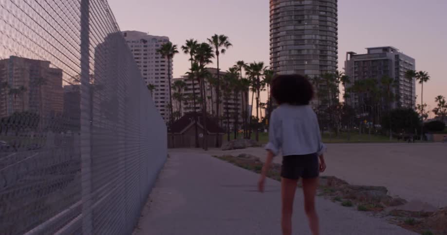 The woman roller skates past the fence at sunset