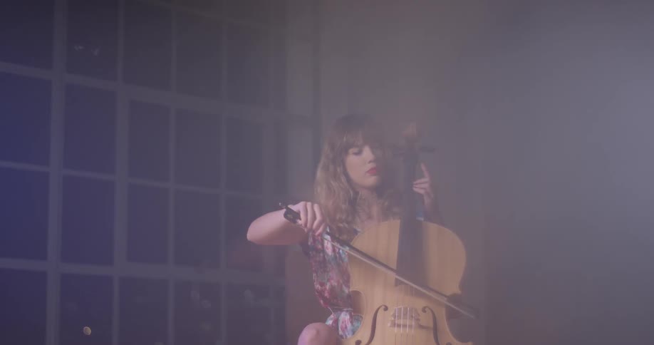 A woman plays a cello in front of a window