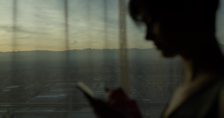 Woman touches the screen of her cellphone as she stands near a window