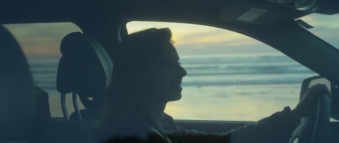 A woman drives on a beach at sunset