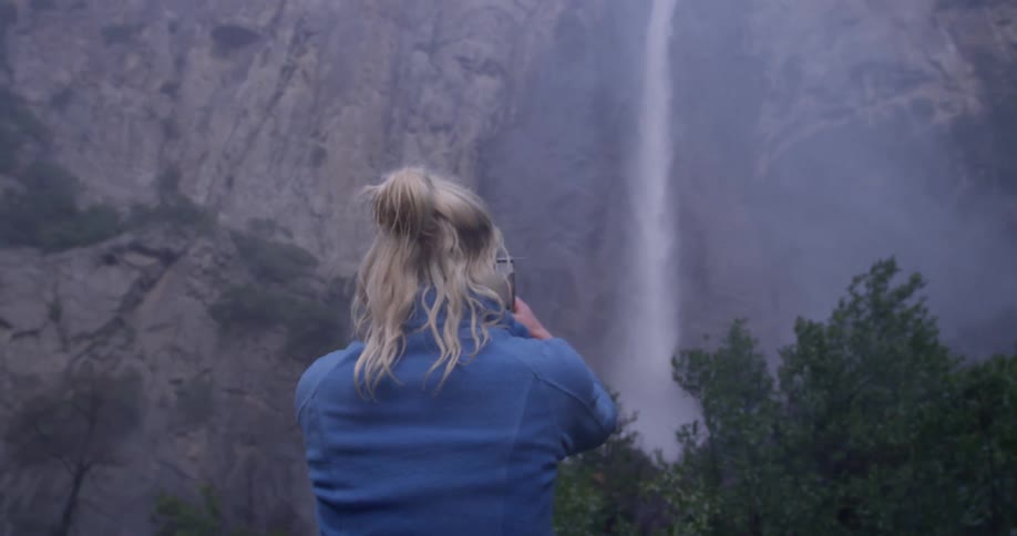 Woman takes a picture of a large waterfall with her phone