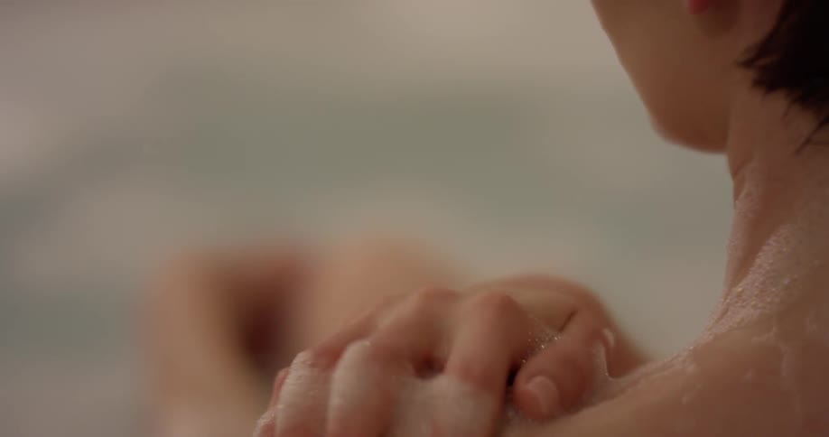 A woman wipes soap and bubbles on her neck in the tub
